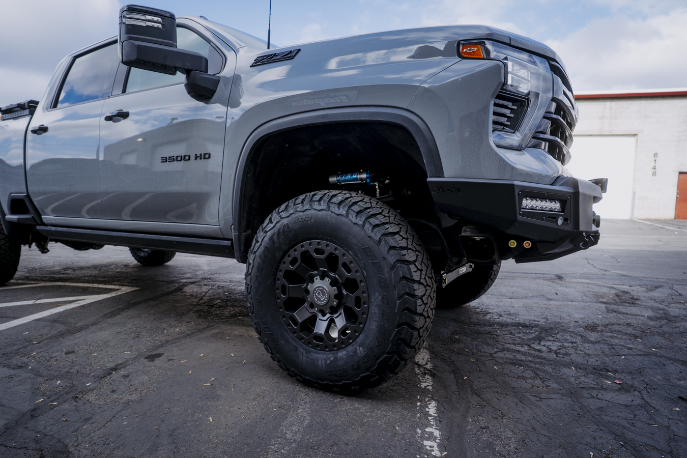 Front quarter view of 2024 Chevy Silverado with suspension lift, front bumper, new tires, and wheels.